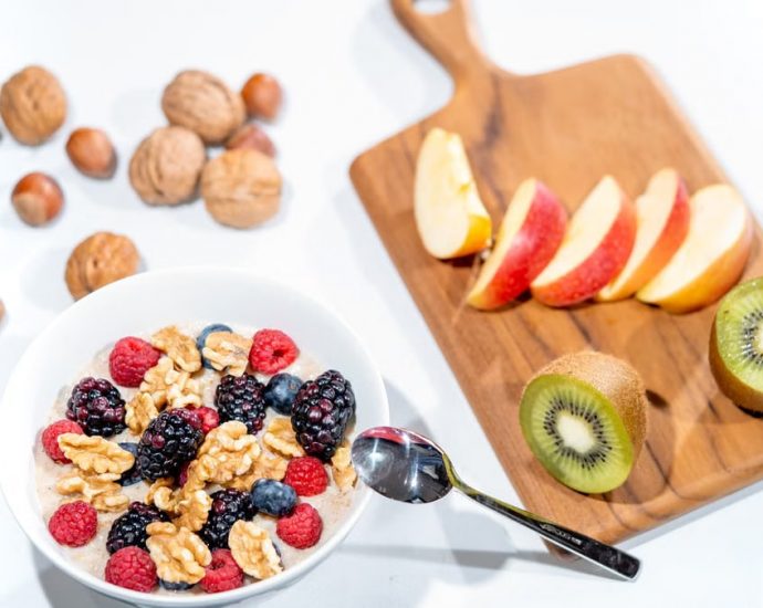 A nutritious breakfast bowl featuring fresh berries and walnuts, served with sliced fruit and kiwi.